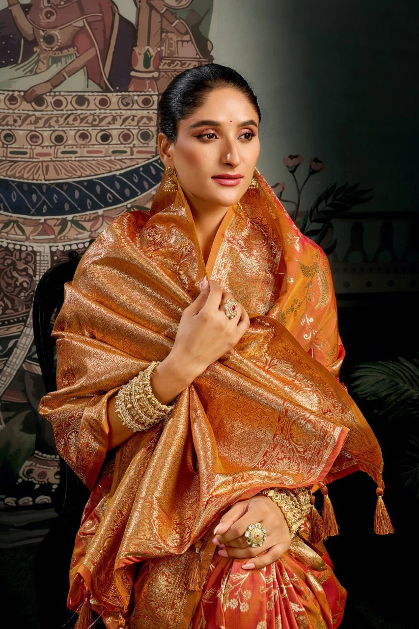 Woman wearing a traditional orange saree with intricate patterns in a decorative setting.